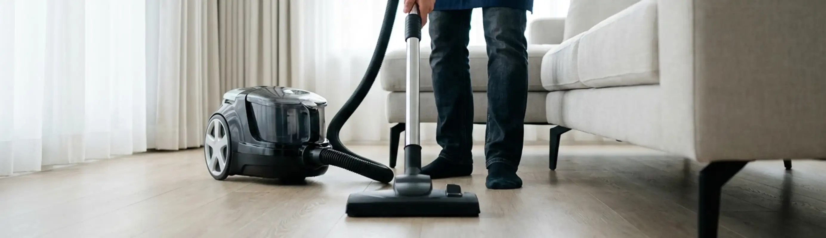 Professional house cleaner vacuuming a living room floor with a canister vacuum cleaner, Los Angeles, CA.