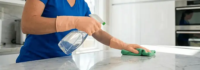 Maid service worker spraying and wiping a kitchen countertop with a microfiber cloth for sanitizing, Los Angeles, CA.