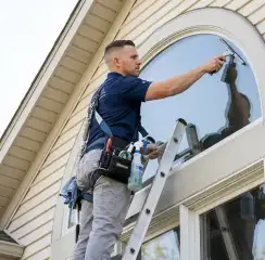 Professional window cleaner on a ladder using a squeegee to clean an exterior arched window, Los Angeles, CA.