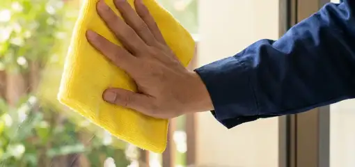 House cleaner wiping a glass window with a yellow microfiber cloth for streak-free cleaning, Los Angeles, CA.